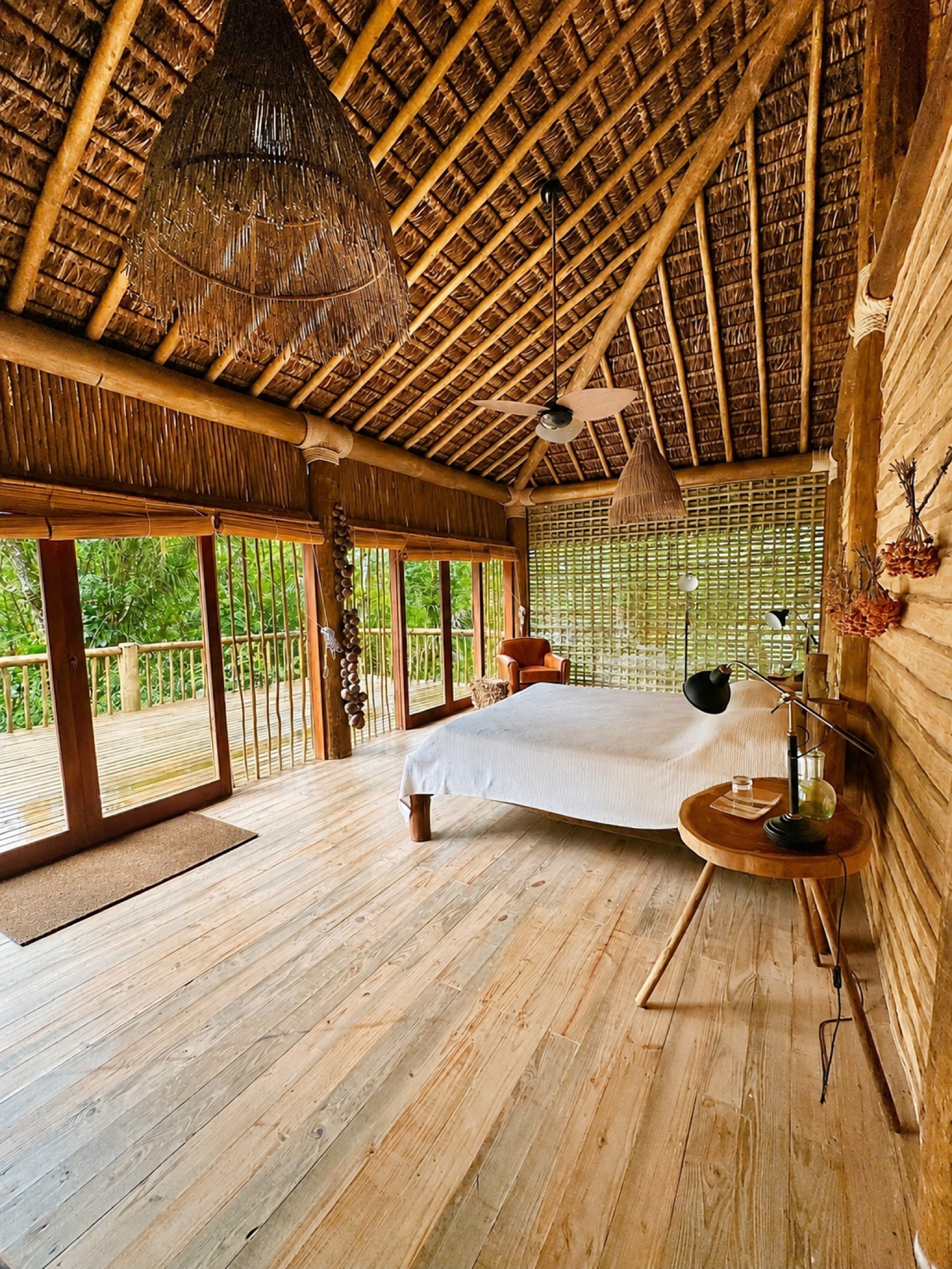Wooden bedroom with thatched ceiling and forest-facing doors